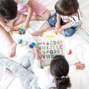 birds eye view of three children playing on a bed with puzzles and toys